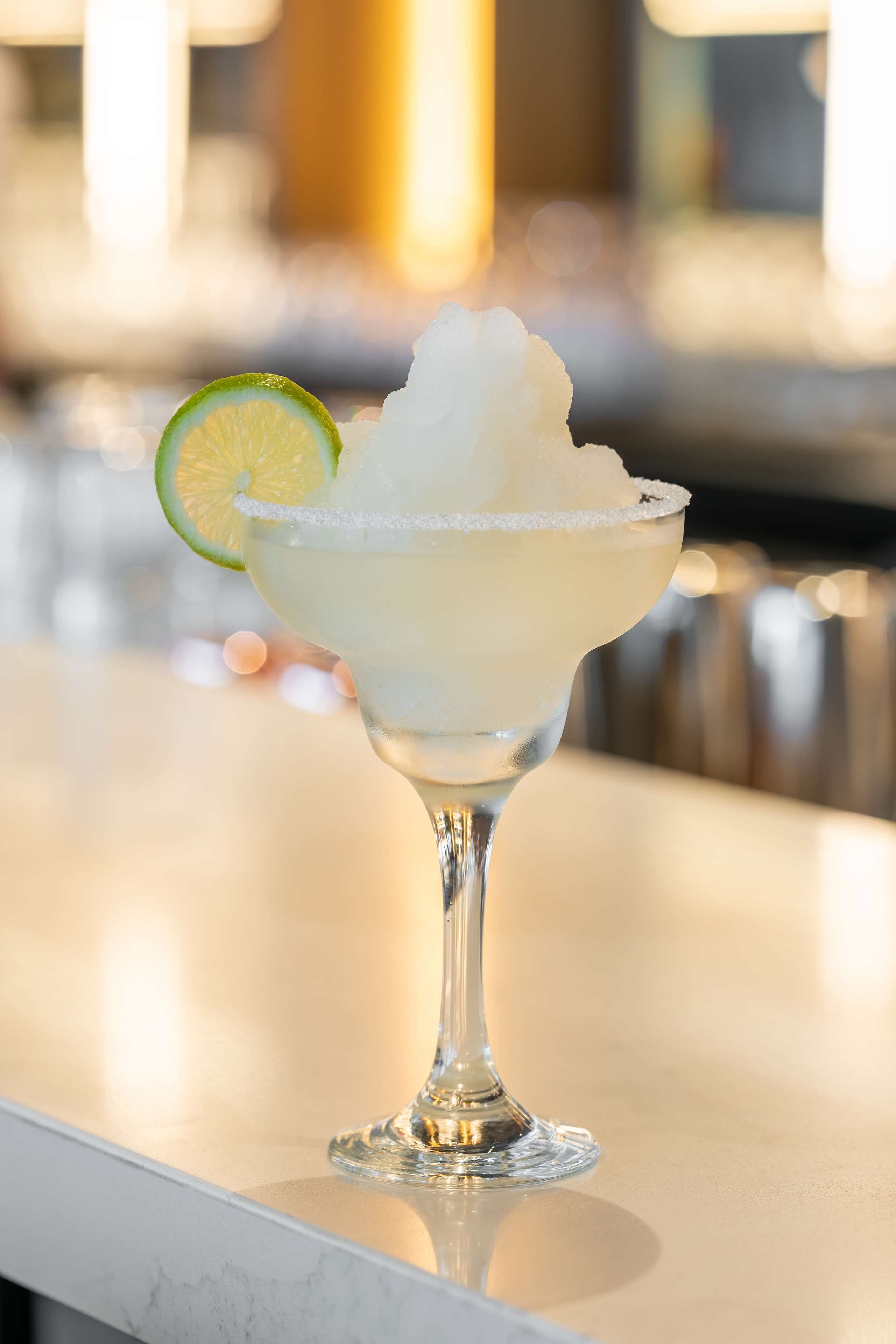 A margarita with ice and a lime slice on a bar counter.
