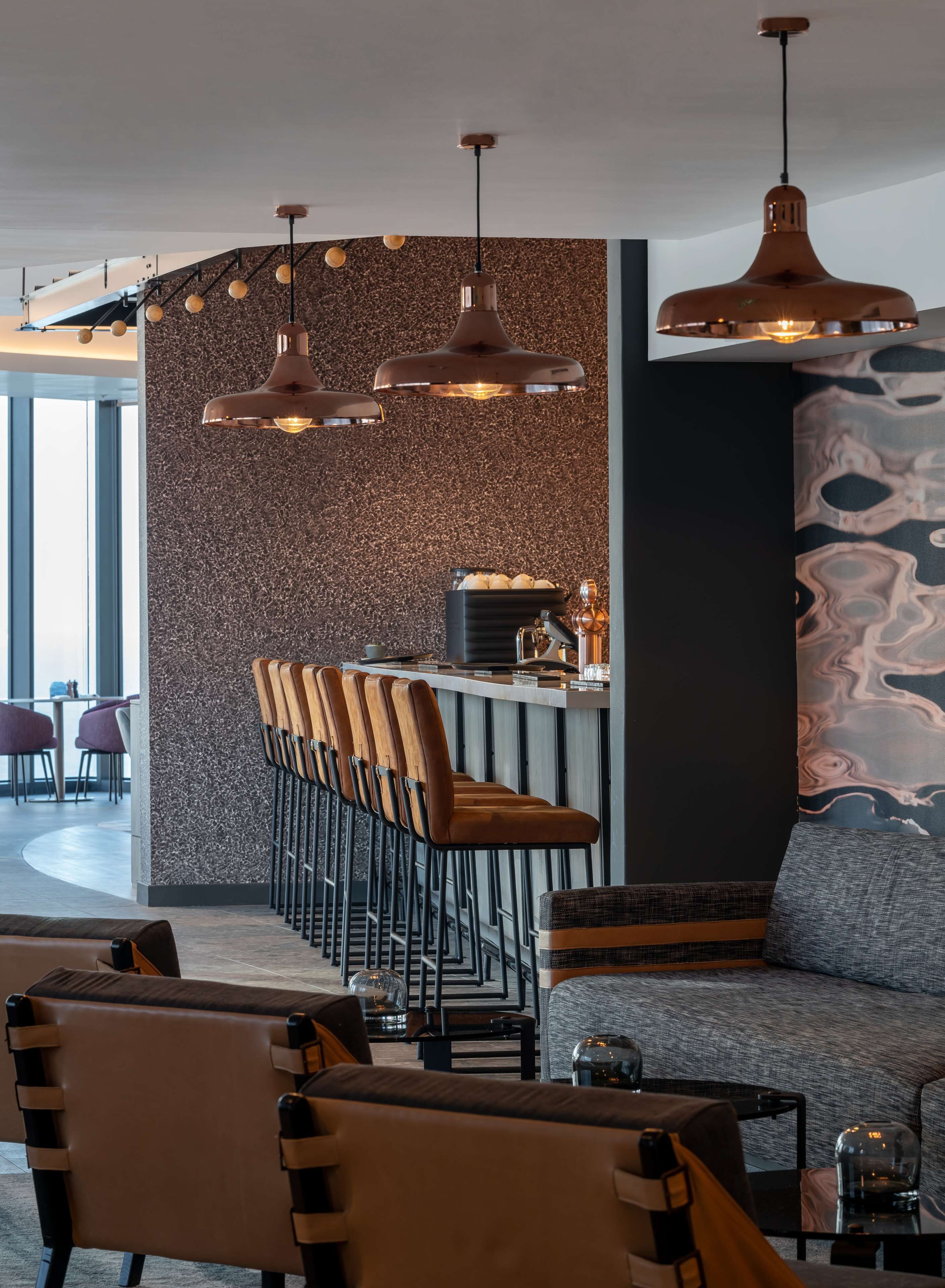 A modern bar area with a high bar counter, multiple stools, and pendant lighting.