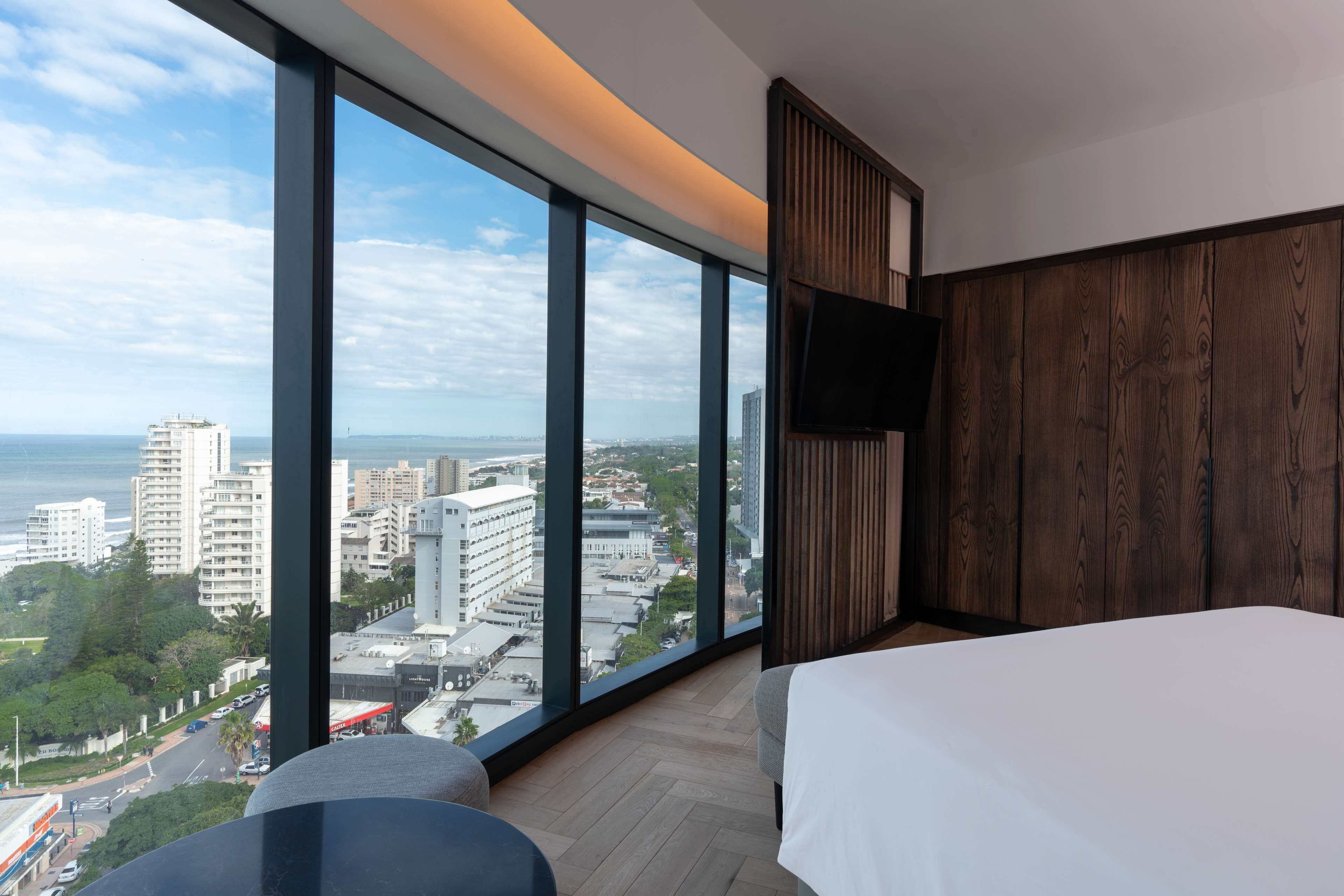 A hotel room with a large window, a bed, a flat-screen TV, and a view of the cityscape.