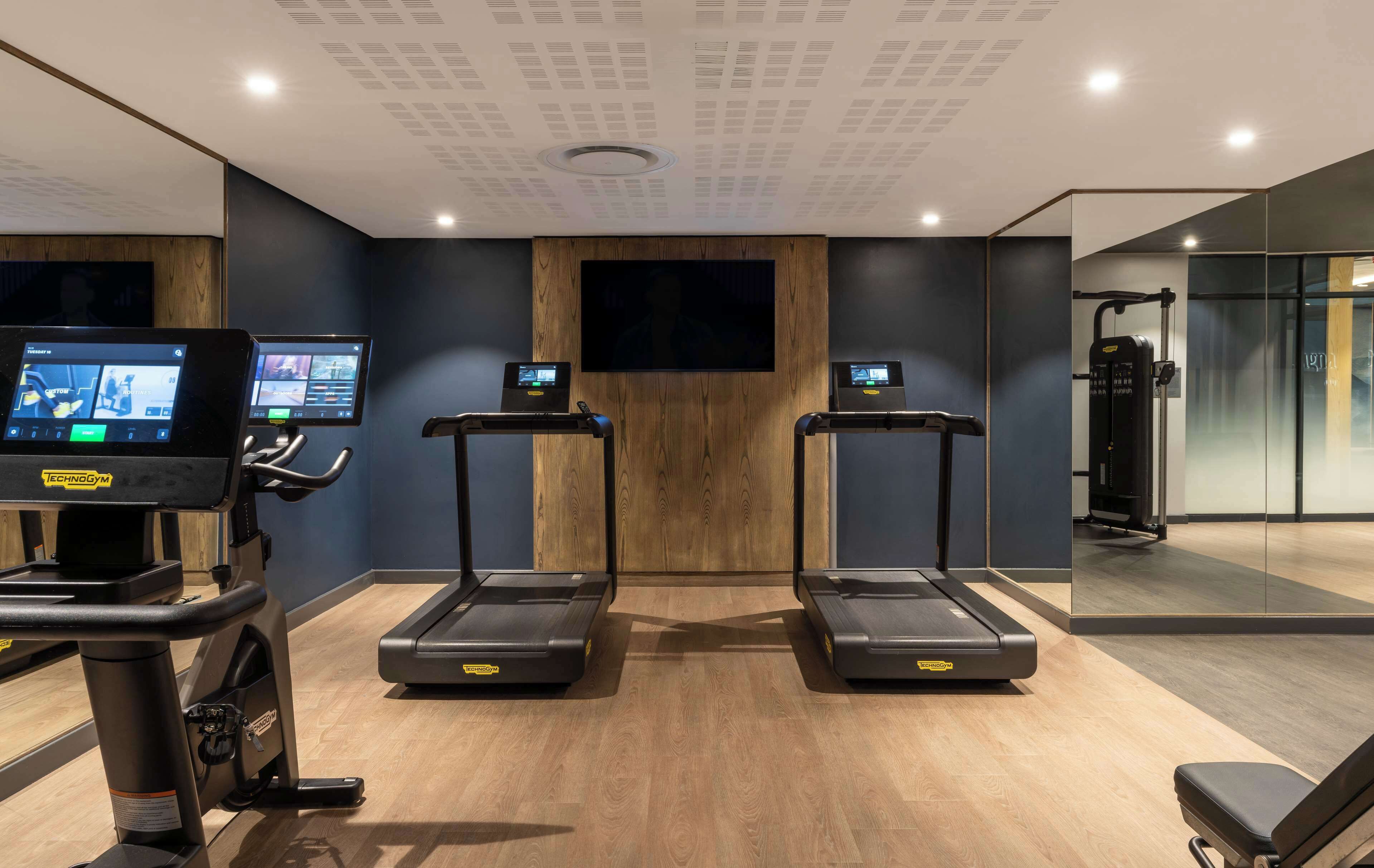 Un gimnasio con cintas de correr, una bicicleta estática y una pantalla de televisión mostrando videos de ejercicios.