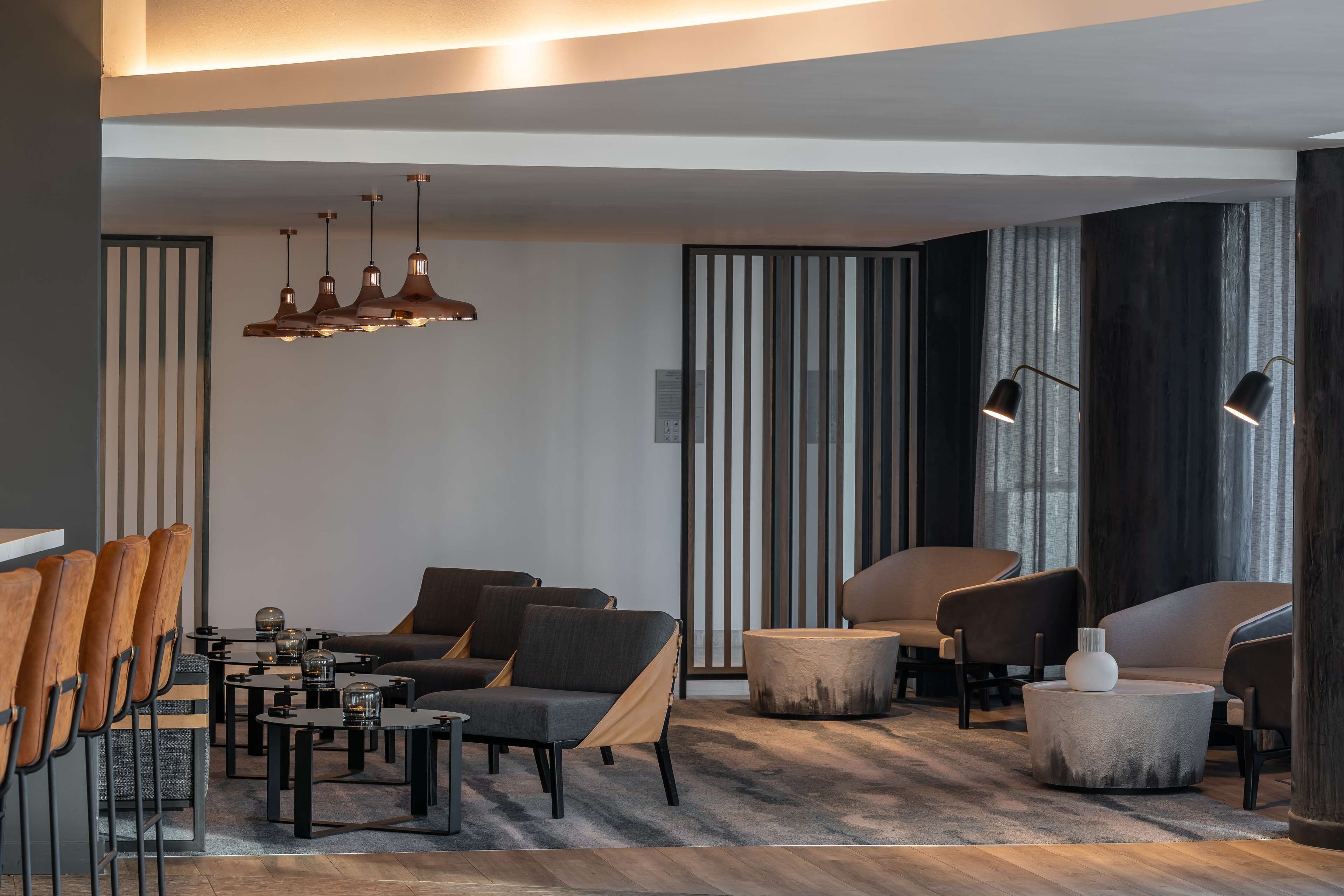 Een moderne woonkamer met een zithoek, salontafel en stoelen. Er zijn hanglampen en een vloerlamp.