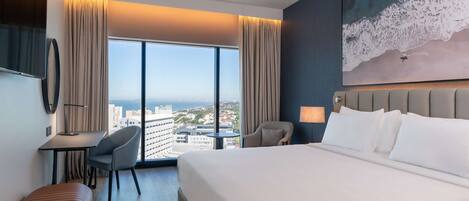 Habitación de hotel con una cama grande, un escritorio, una silla y vistas a la ciudad.