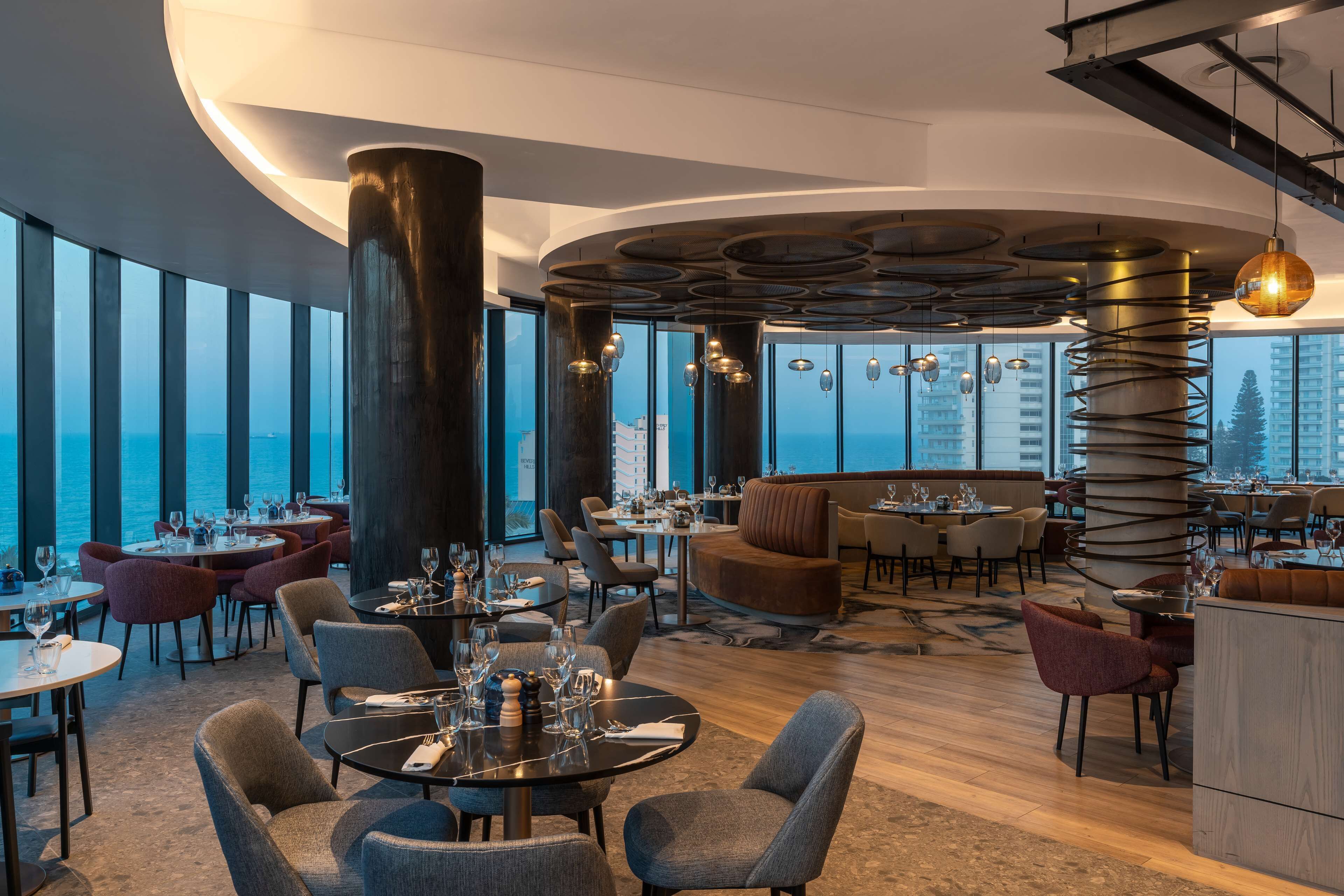 Un restaurant moderne avec des tables rondes, des sièges confortables et de grandes fenêtres donnant sur la ville.