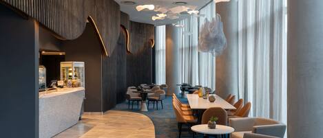 A modern hotel lobby with a reception desk, seating area, and large windows.