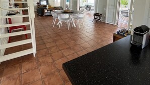 Un amplio espacio habitable con techo alto, una mesa de comedor con sillas, una zona de cocina y una escalera que sube a un nivel superior.