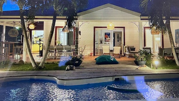 Una casa con piscina, palmeras y zona de comedor.