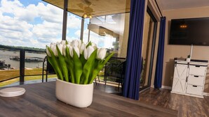 A room with a view of a river, a white vase with green leaves, a TV, and a white cabinet. - Lovely Lake Hamilton Condo, 1BR, Main Channel with an AMAZING VIEW! w/ boat slip (Hot Springs)