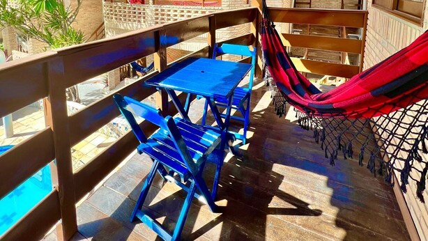 An outdoor patio with a wooden table and chairs, a hammock, and a view of a brick building. - Pousada Porto Henrris (Ipojuca)