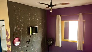 A bedroom with a bed, a ceiling fan, a wall-mounted TV, a mirror, a window with curtains, and a wall with a leaf pattern. - HOTEL NEVADA (Ubatuba)