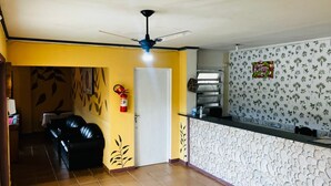 A hotel lobby with a reception desk, a black leather sofa, a ceiling fan, and a fire extinguisher. - HOTEL NEVADA (Ubatuba)