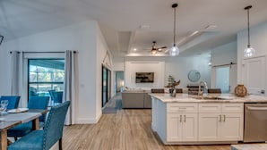 Een moderne keuken met witte kastjes, een eethoek met blauwe stoelen en een groot raam.