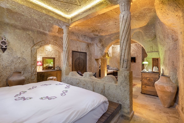 A stone-walled room with a bed, a wooden dresser, and a large vase. - Kayata Cave Suites (Ürgüp)