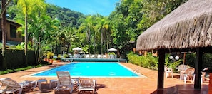 A swimming pool with lounge chairs and a thatched-roof structure.