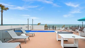 A rooftop terrace with lounge chairs, a table, and a view of the ocean. - Tropic Sun Towers (Ormond Beach)