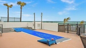 A shuffleboard table on a rooftop with a view of the ocean and palm trees. - Tropic Sun Towers (Ormond Beach)
