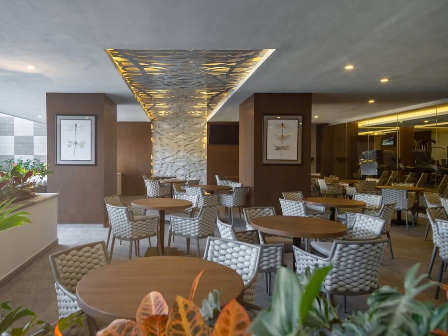 Un comedor interior moderno con mesas redondas y sillas de mimbre, destacando un diseño de techo único y obras de arte enmarcadas en las paredes.