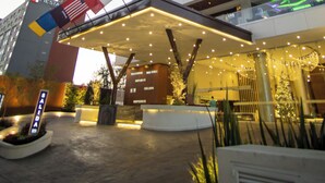 A modern hotel with a prominent entrance, multiple flags, and a well-lit outdoor area. - Sheraton Guadalajara Expo (Zapopan)