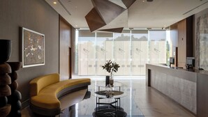 A modern lobby with a curved yellow sofa, a glass coffee table, and a large window with a view of trees. - Sheraton Guadalajara Expo (Zapopan)
