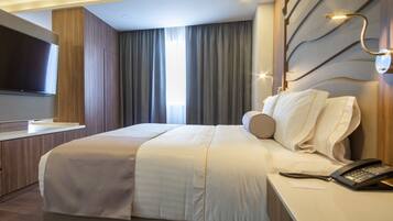 Ein modernes Hotelzimmer mit einem großen Bett, einem Nachttisch mit Telefon, einem an der Wand montierten Flachbildfernseher und einem Fenster mit Vorhängen.