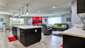 A modern kitchen with a central island, a dining area with chairs, a living room with a sofa and a coffee table, and a kitchen counter with a sink. - Fully licensed pool home w/outdoor kitchen. (Las Vegas)