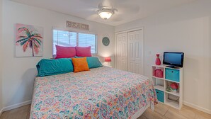 A bedroom with a bed, a ceiling fan, a TV, and a shelf with storage boxes. - Dream Chaser- Walk to Sandfest & Ocean Breeze! Heated Pool & Pets OK (Port Aransas)