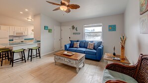 A living room with a blue sofa, a wooden coffee table, and a ceiling fan. - Dream Chaser- Walk to Sandfest & Ocean Breeze! Heated Pool & Pets OK (Port Aransas)