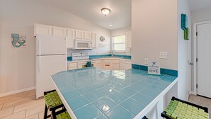 A compact kitchen with white cabinets, a blue-tiled island, and a microwave. - Dream Chaser- Walk to Sandfest & Ocean Breeze! Heated Pool & Pets OK (Port Aransas)
