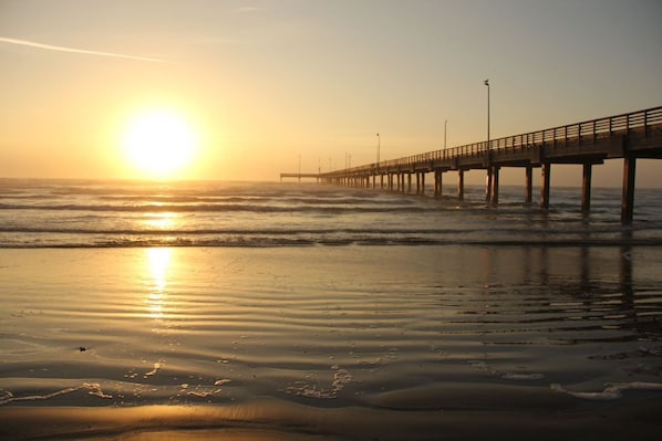 A pier extending into the ocean with the sun setting in the background.