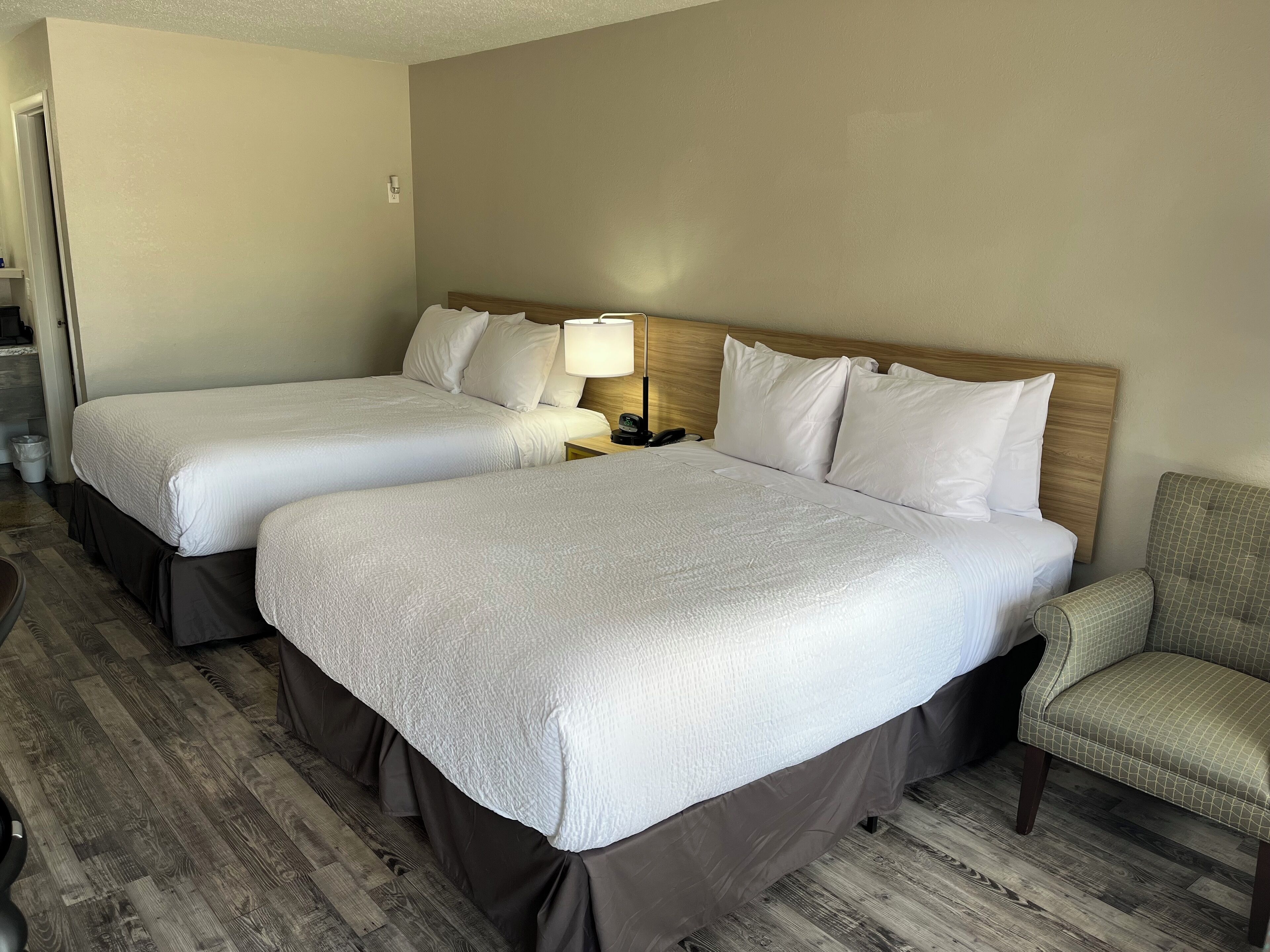 Een hotelkamer met twee bedden, een nachtkastje met lamp, een stoel en een houten vloer.