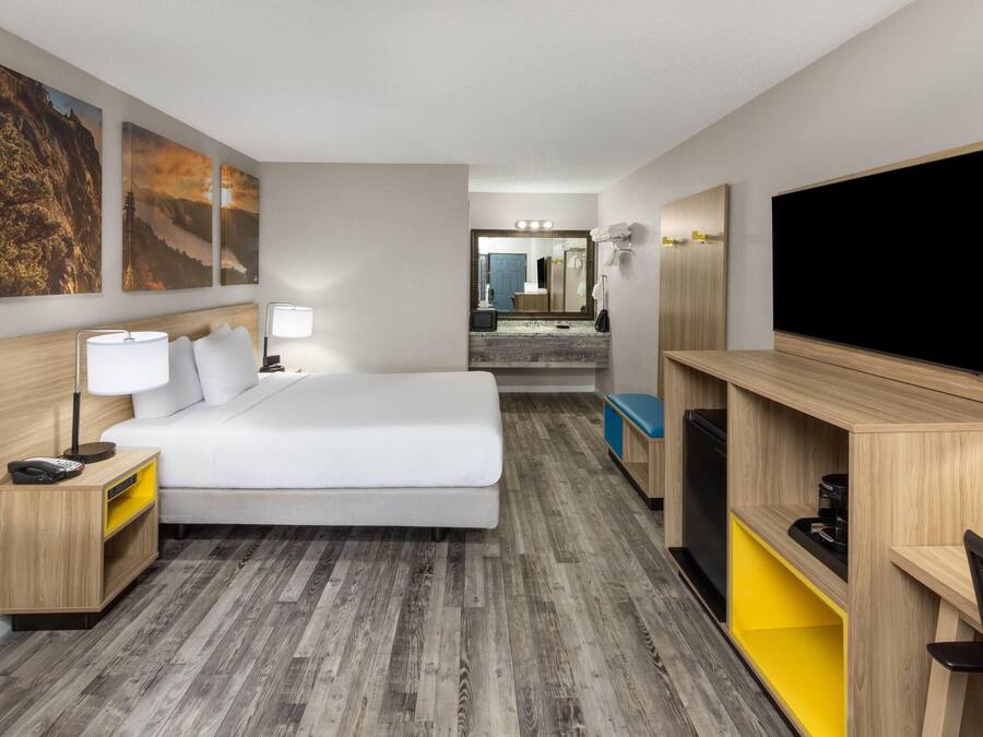 Una camera d'albergo con un letto, comodino, lampada, televisione e una scrivania con una sedia.