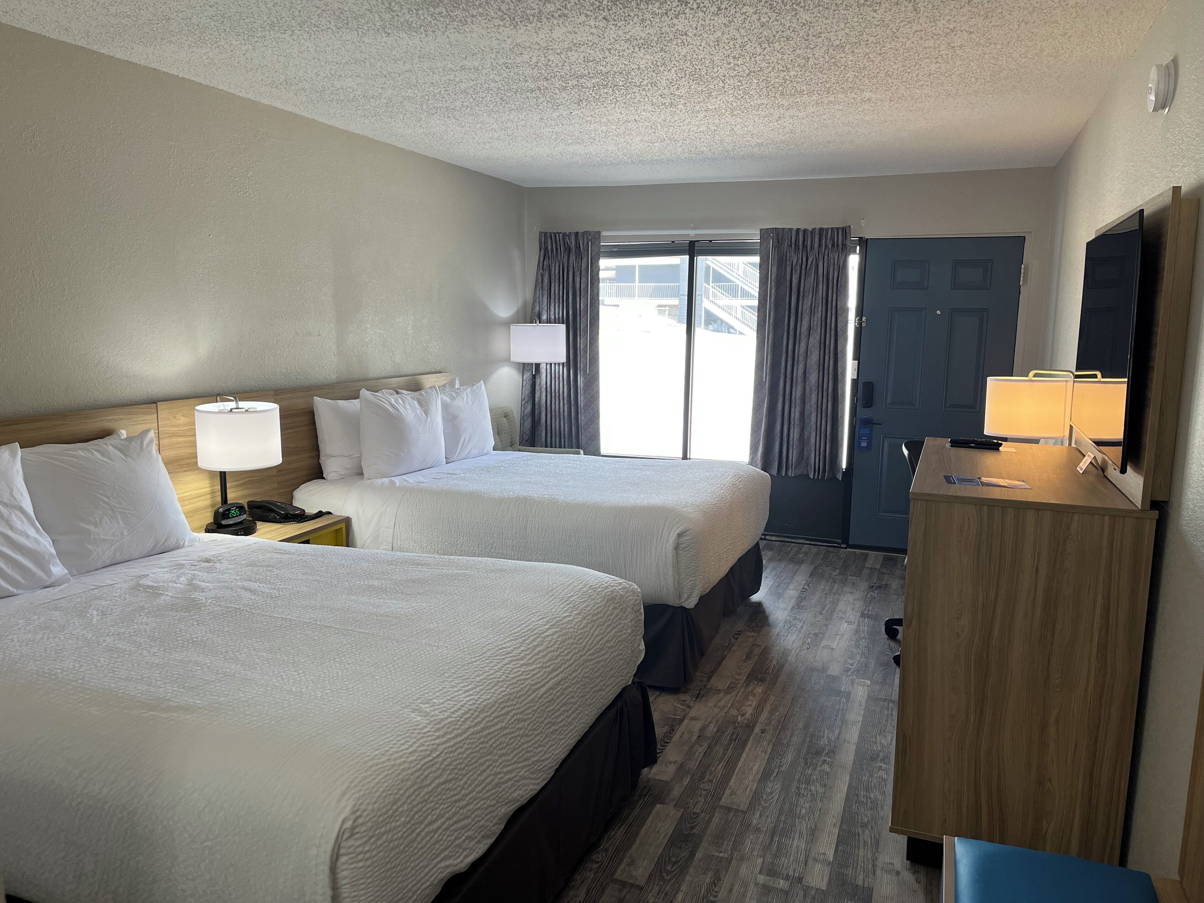 A hotel room with two beds, a desk with a lamp, a TV, and a wardrobe.