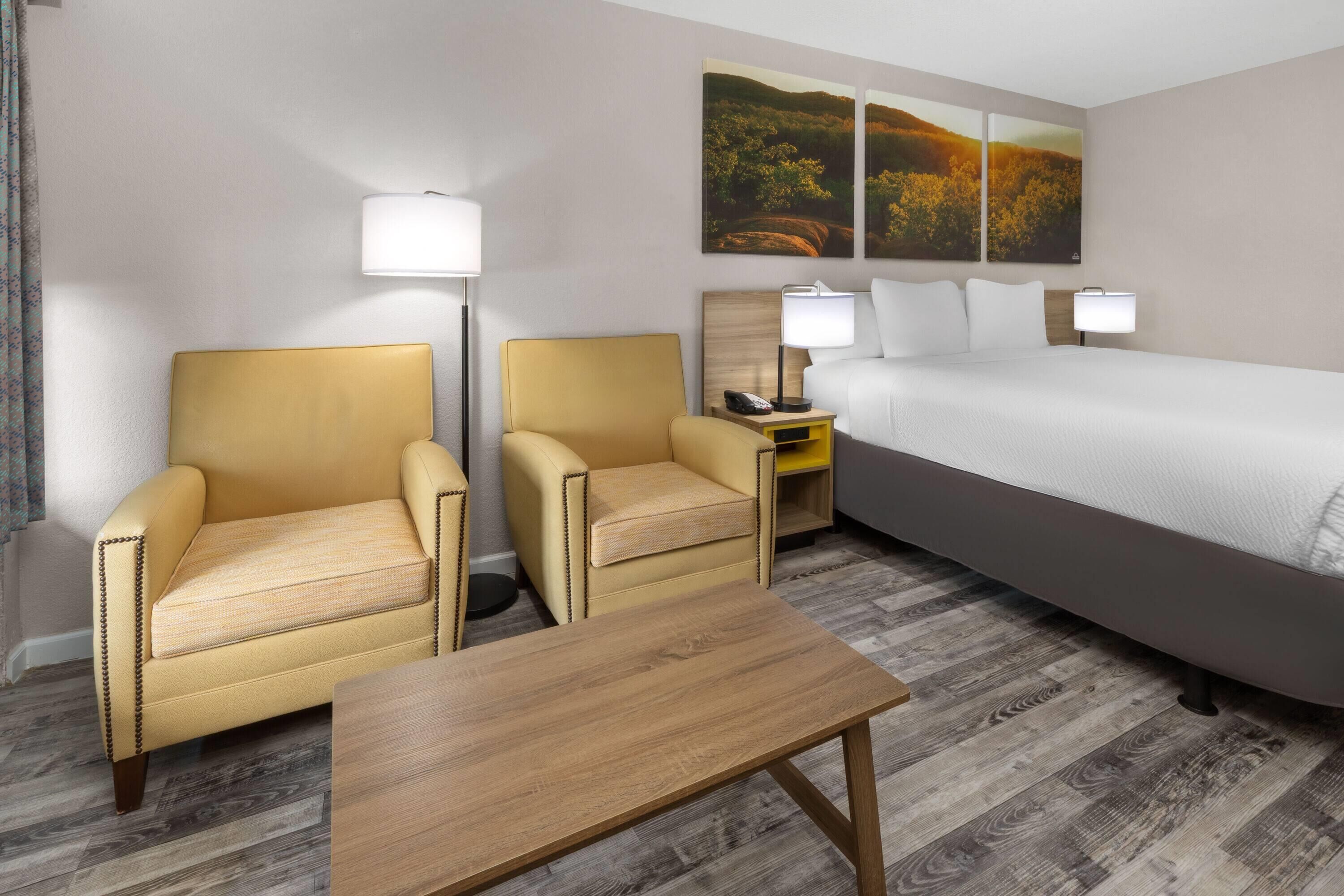 A hotel room with a bed, two armchairs, a small table, and two bedside lamps.