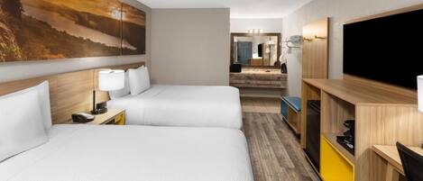 Ein Hotelzimmer mit zwei Betten, einem Fernseher, einem Schreibtisch und einem Badezimmer im Hintergrund.