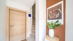 A hotel hallway with a wooden door, a staircase, a sign indicating 'Argentine Rooms', a framed picture on the wall, and a white vase with green plants on a small table. - Argenta Rooms - Premium Double Room with Balcony (Dubrovnik)