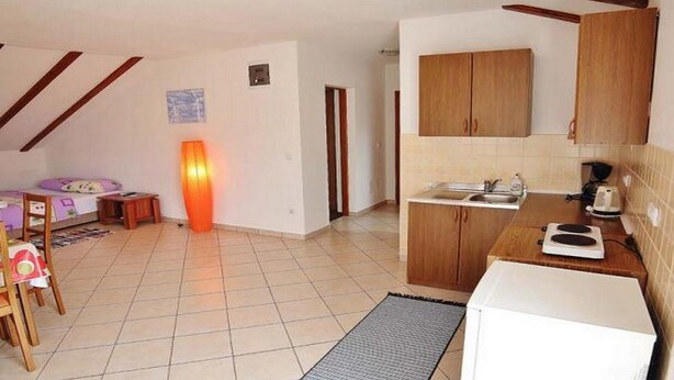 Una habitación pequeña y luminosa con cama, escritorio y kitchenette.