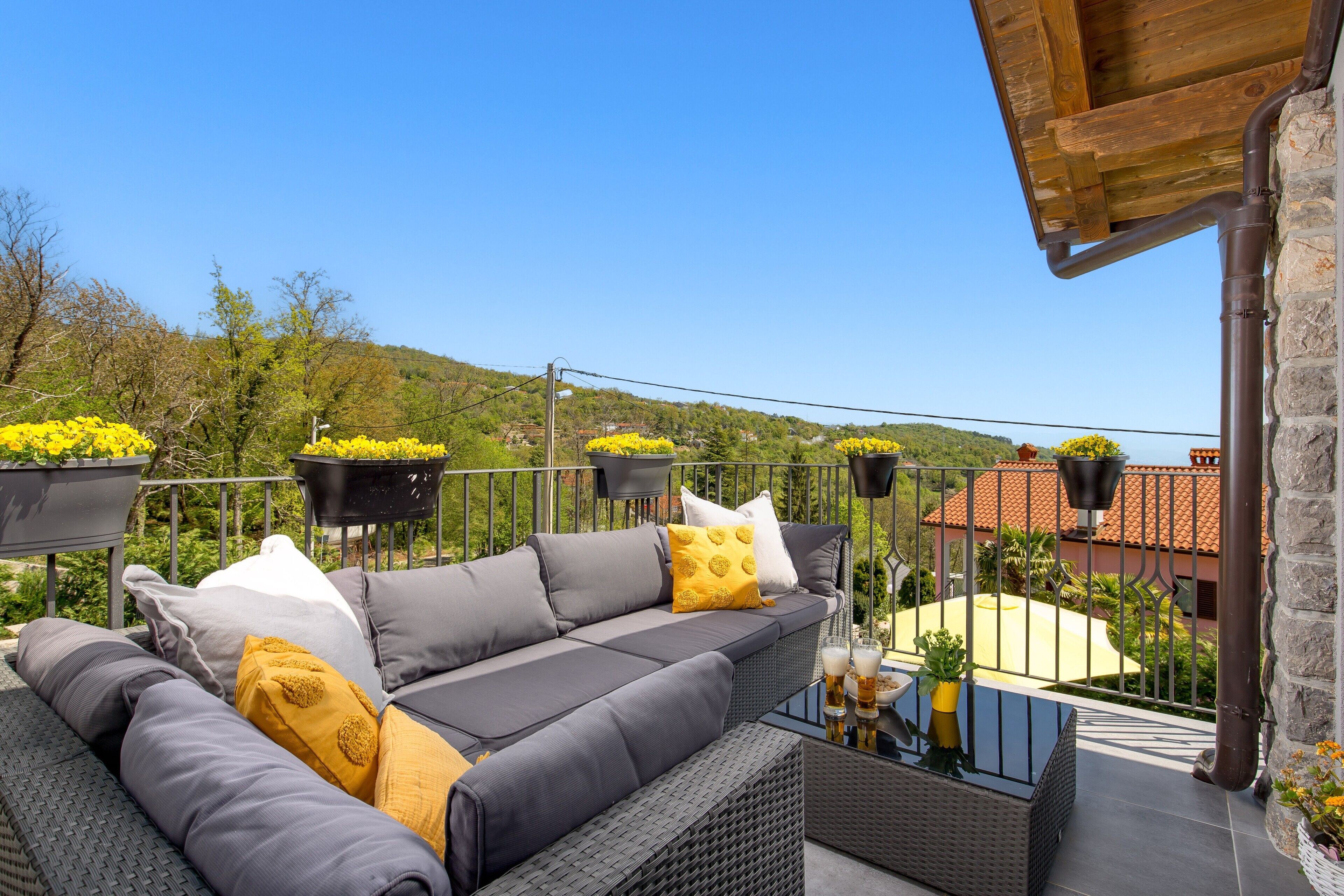 A balcony with a grey sofa, yellow cushions, and black planters with yellow flowers.
