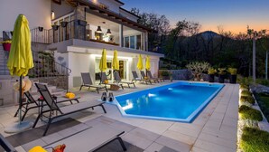 Ett modernt hus med en swimmingpool, utomhusmöbler och en välskött trädgård.