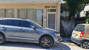 En grå SUV parkeret foran en bygning med et skilt, der siger "SAK NAJ".