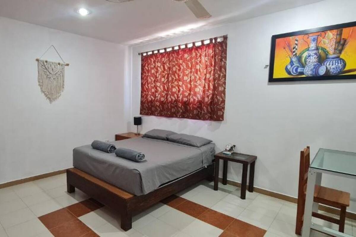Une chambre à coucher comprenant un lit, une télévision, un petit réfrigérateur, une table de chevet, une table en verre et une chaise.