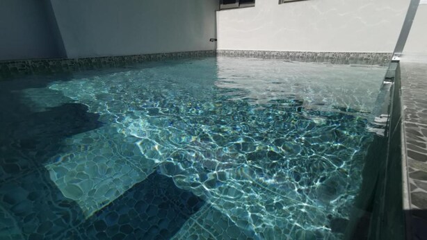 En lys swimmingpool indendørs med flisegulv og vægge.