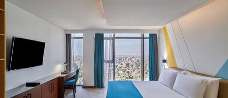 Habitación de hotel con una cama grande, un escritorio con computadora, un televisor de pantalla plana y vista a la ciudad.
