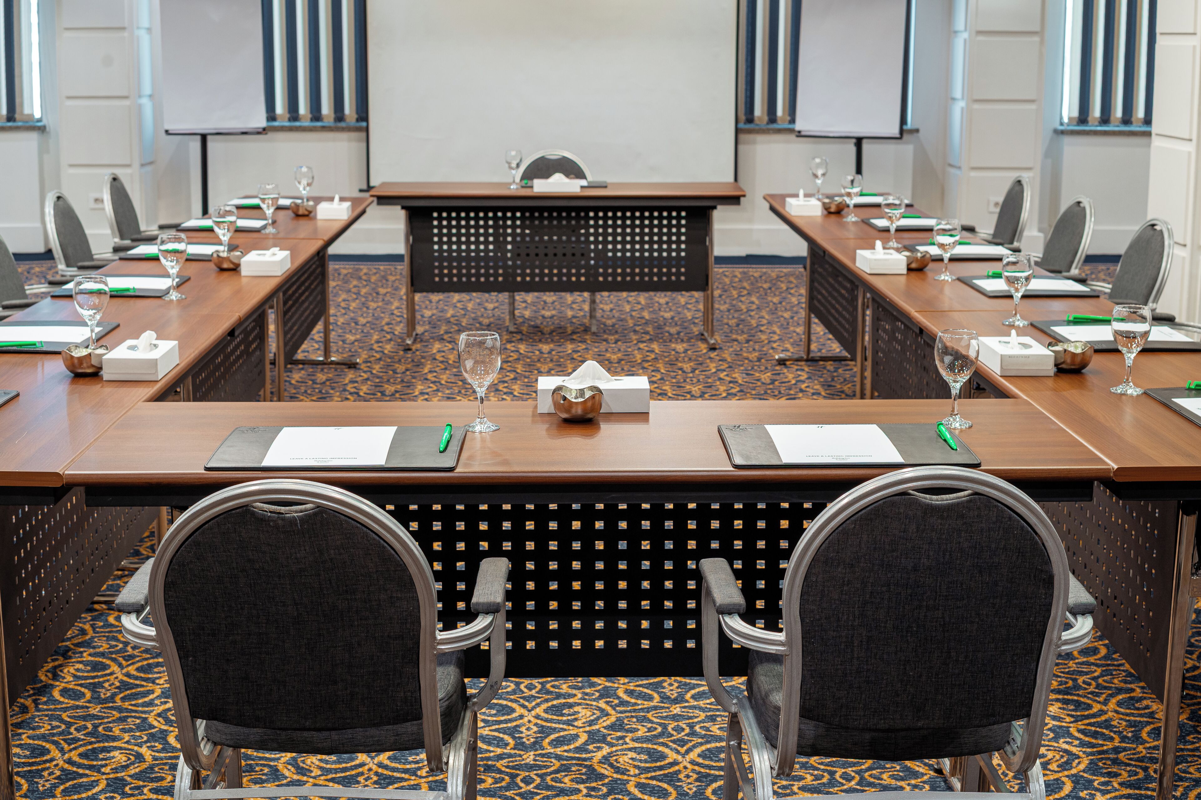 A conference room with a long table, chairs, a projector screen, and a carpeted floor.