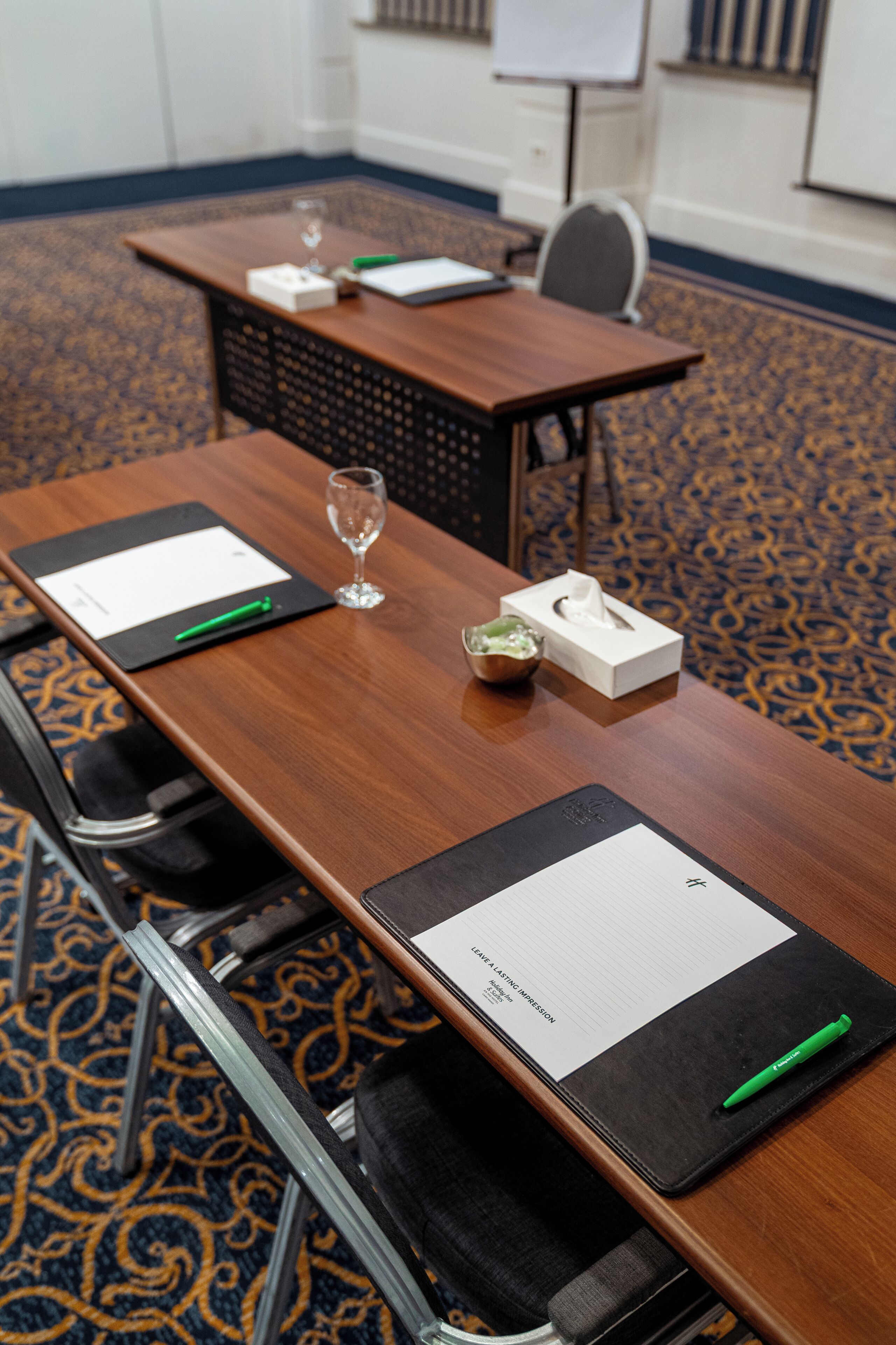 Une salle de conférence avec une longue table, des chaises, un tableau blanc et une moquette à motifs.