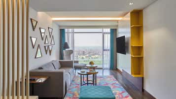 Una sala moderna con un sofá, una mesita, un tapete colorido y vistas a un paisaje urbano a través de amplios ventanales.