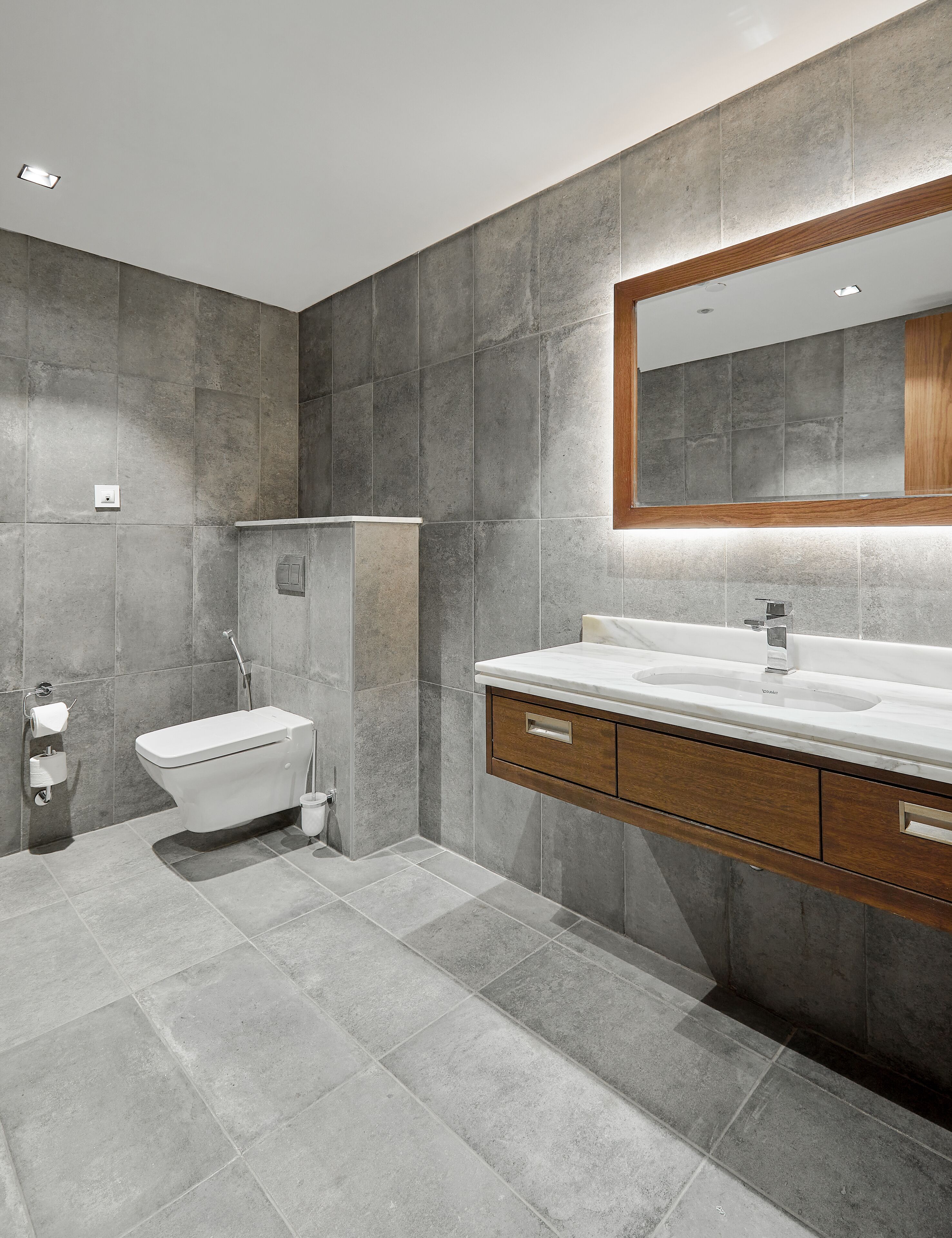 A modern bathroom with a built-in toilet, a sink with a wooden vanity, and a large mirror.