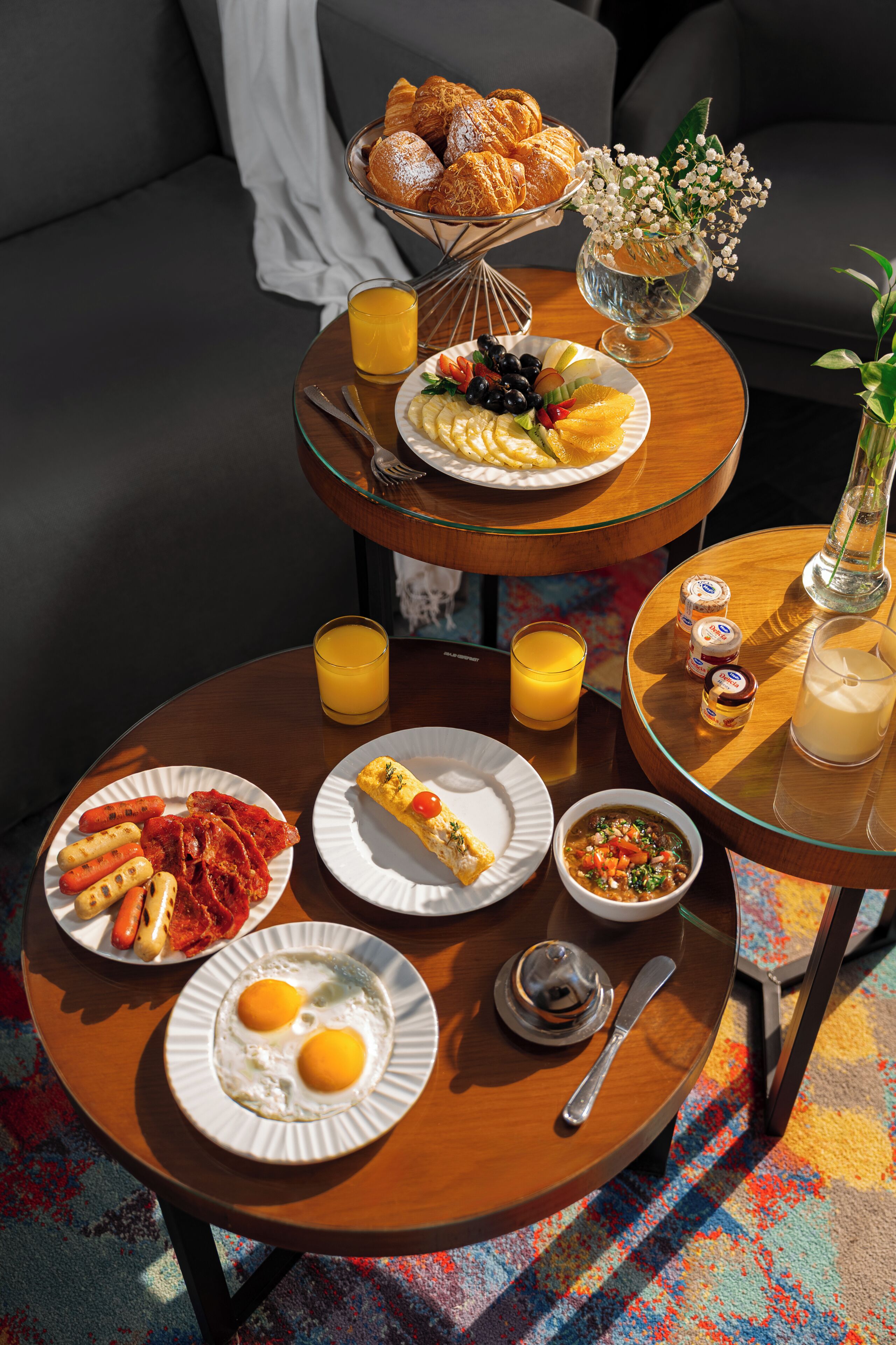 A breakfast table with croissants, fruit, eggs, and a vase of flowers.