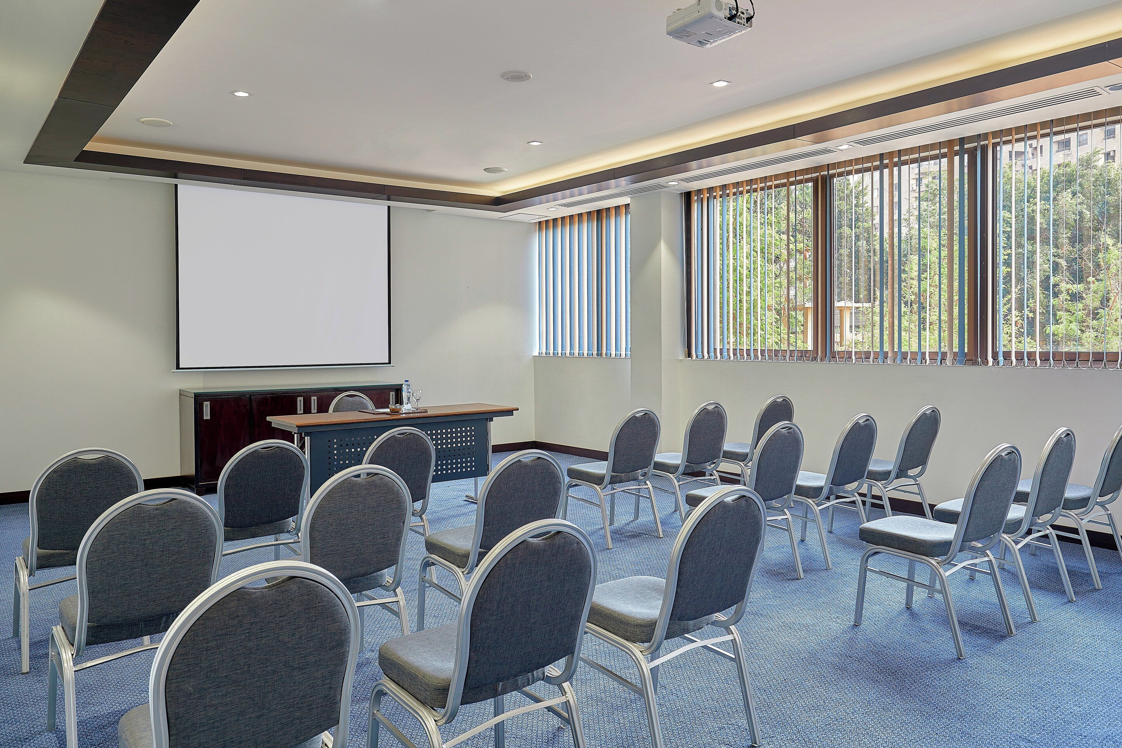 Un salón de conferencias con hileras de sillas, una pantalla para proyector y un atril.