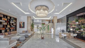 En moderne lobby med en central lysekrone, siddeområder og en receptionsdisk.