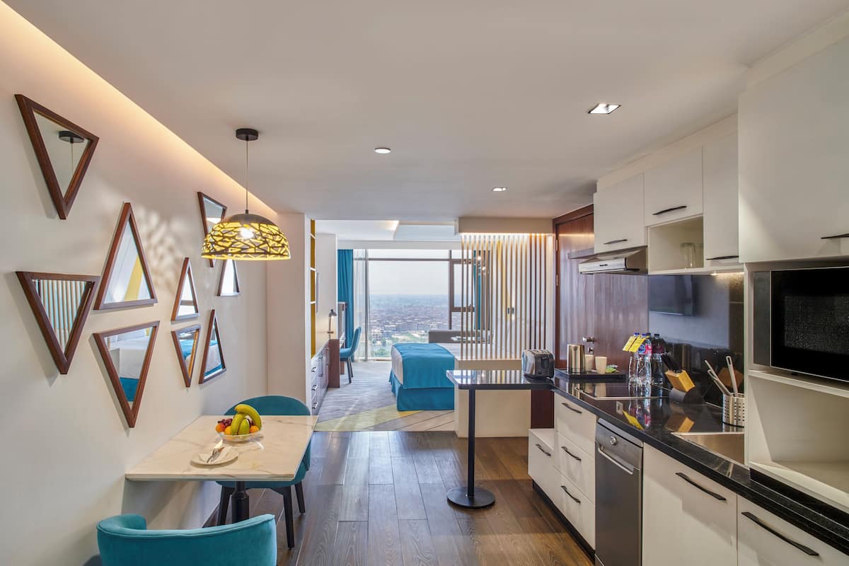 A modern kitchen with a dining area, a view through the window, and a living space with a bed.