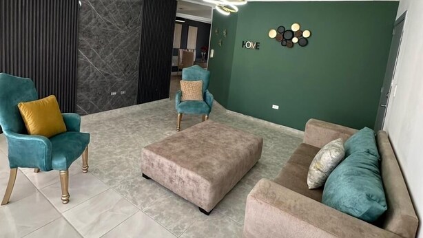 Ein modernes Wohnzimmer mit blaugrünen und beigen Möbeln, einem Marmorboden und einer grünen Akzentwand.